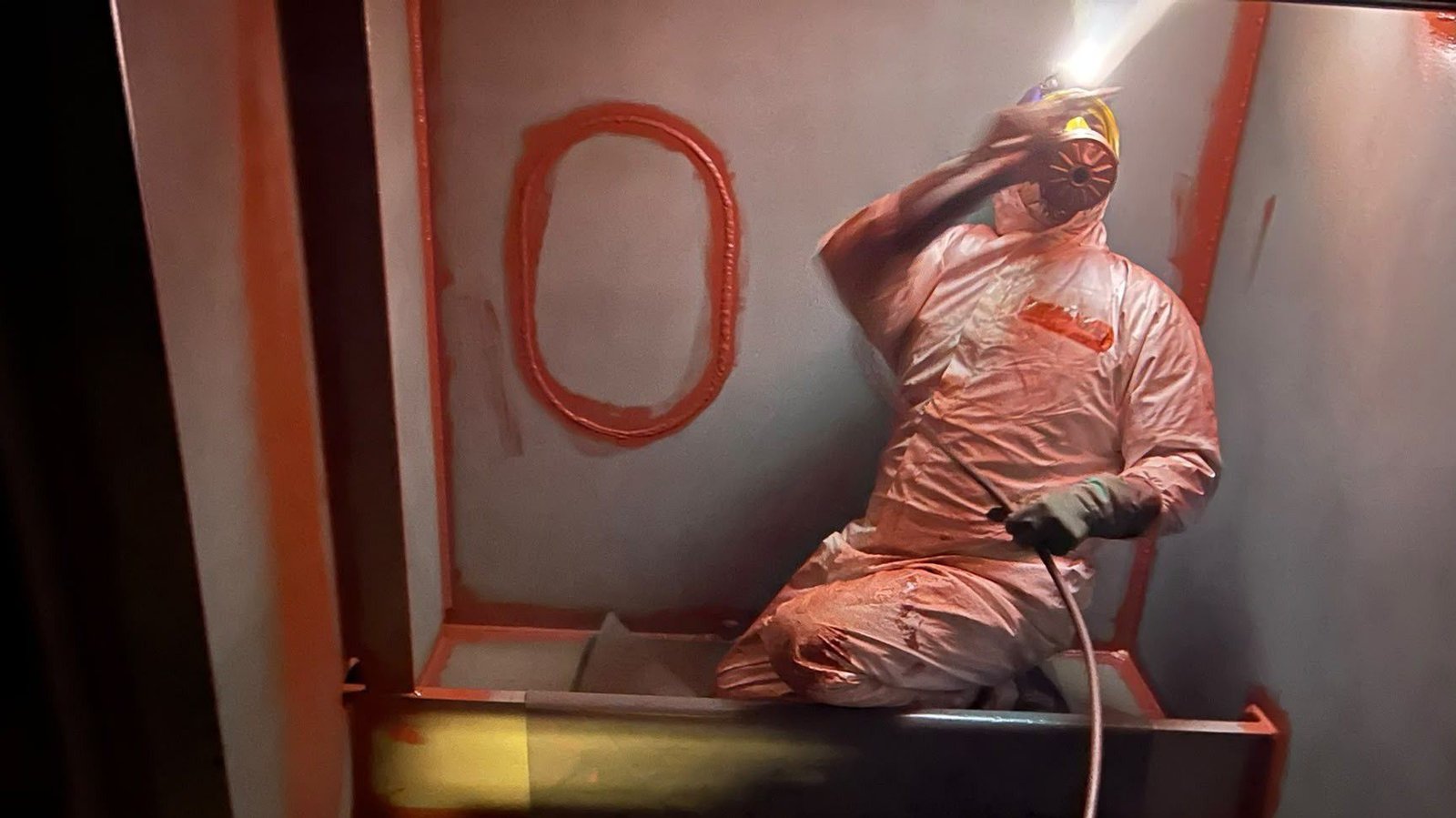 Technician applying protective coating inside an industrial steel enclosure.
