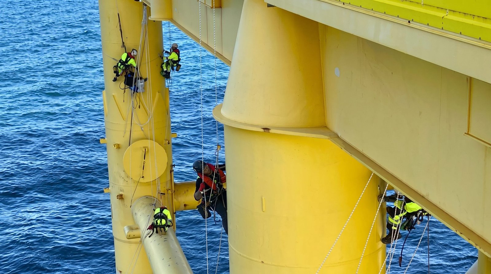 A team of rope access technicians working together on an offshore foundation structure above the sea.