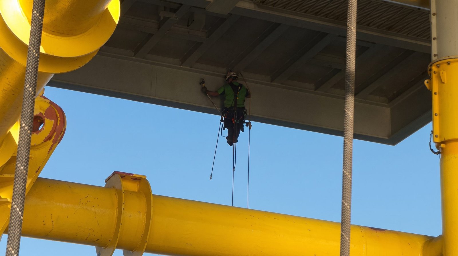 Rope access technician working at a difficult-to-reach area beneath an offshore platform structure.
