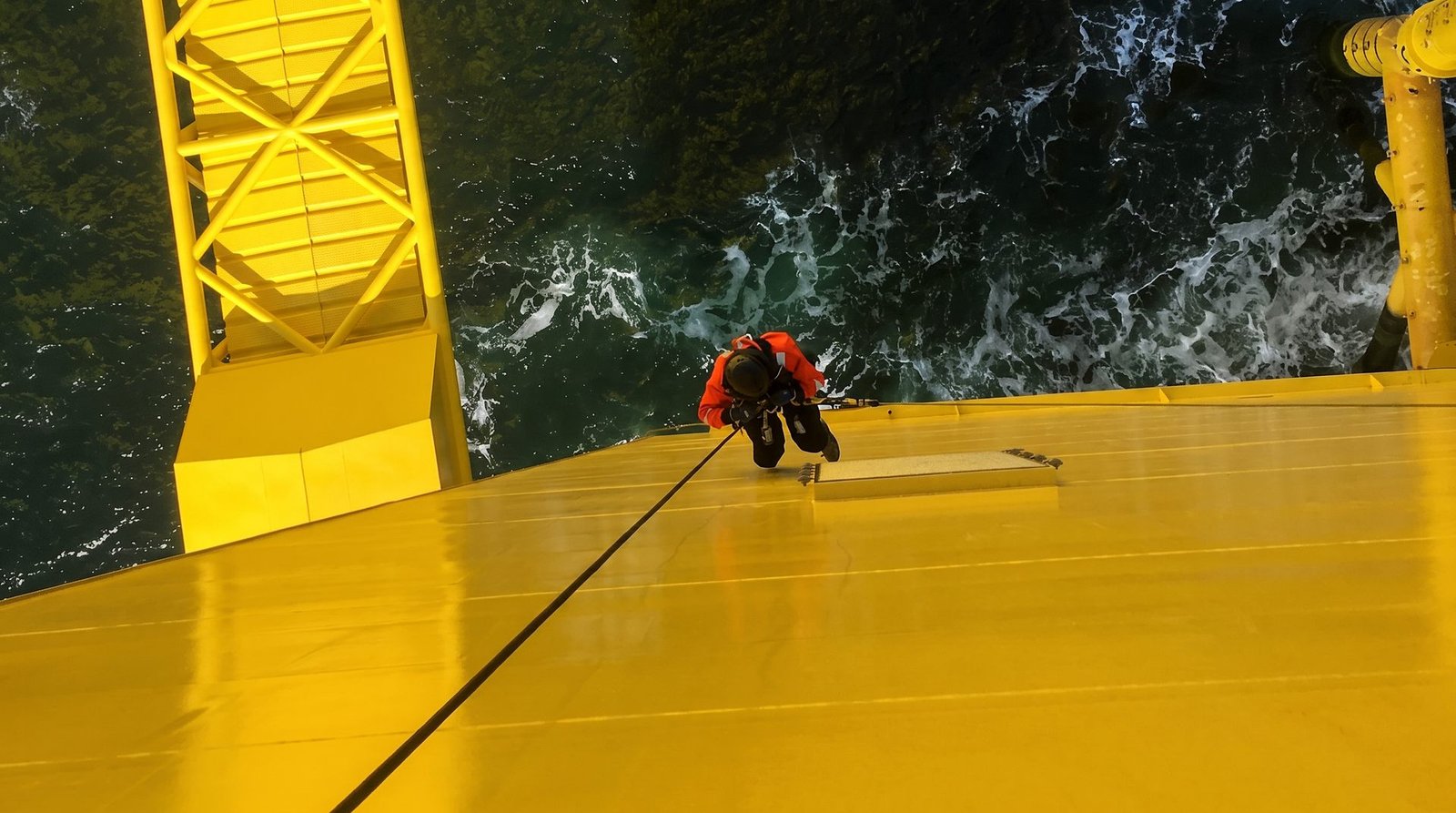 Rope access technician working on a yellow offshore steel structure above the sea.