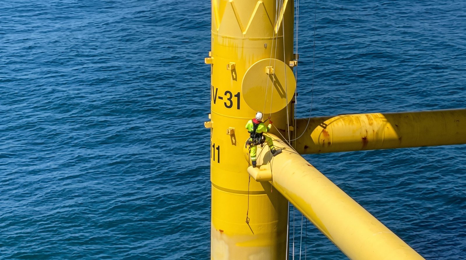 Rope access technicians working on an offshore support structure above open water.