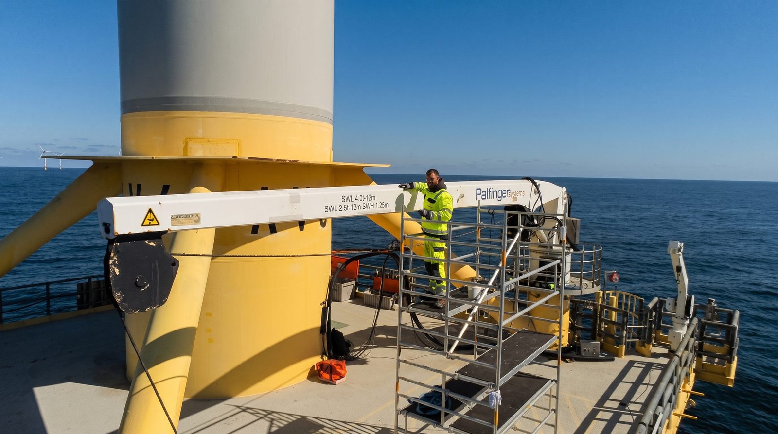 Technician performing maintenance work on an offshore wind platform next to an access crane.