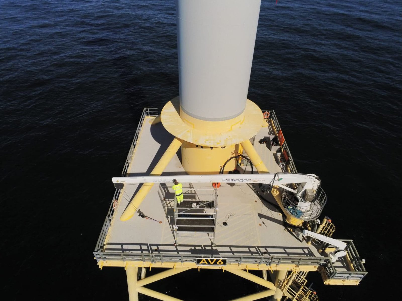 Technician on an offshore wind turbine transition piece platform using an access lift for maintenance work.