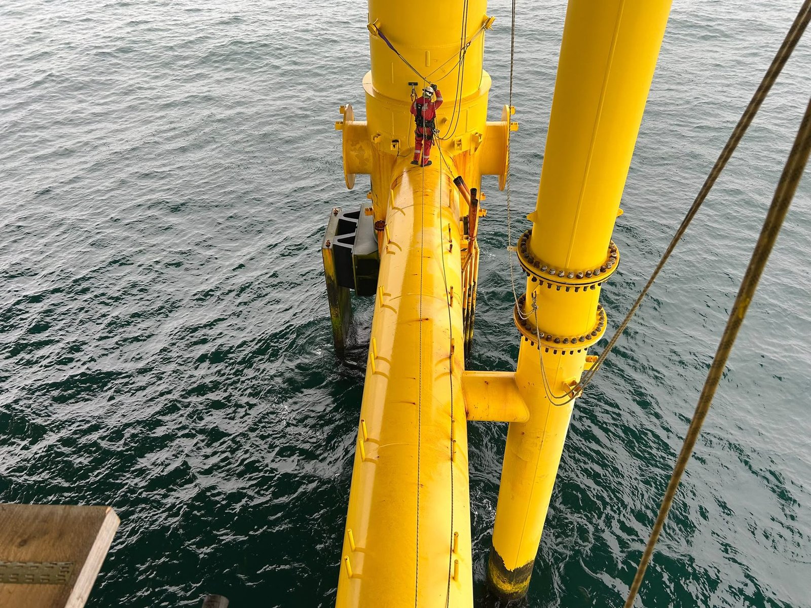 Rope access technician working on a yellow offshore support structure above the sea.