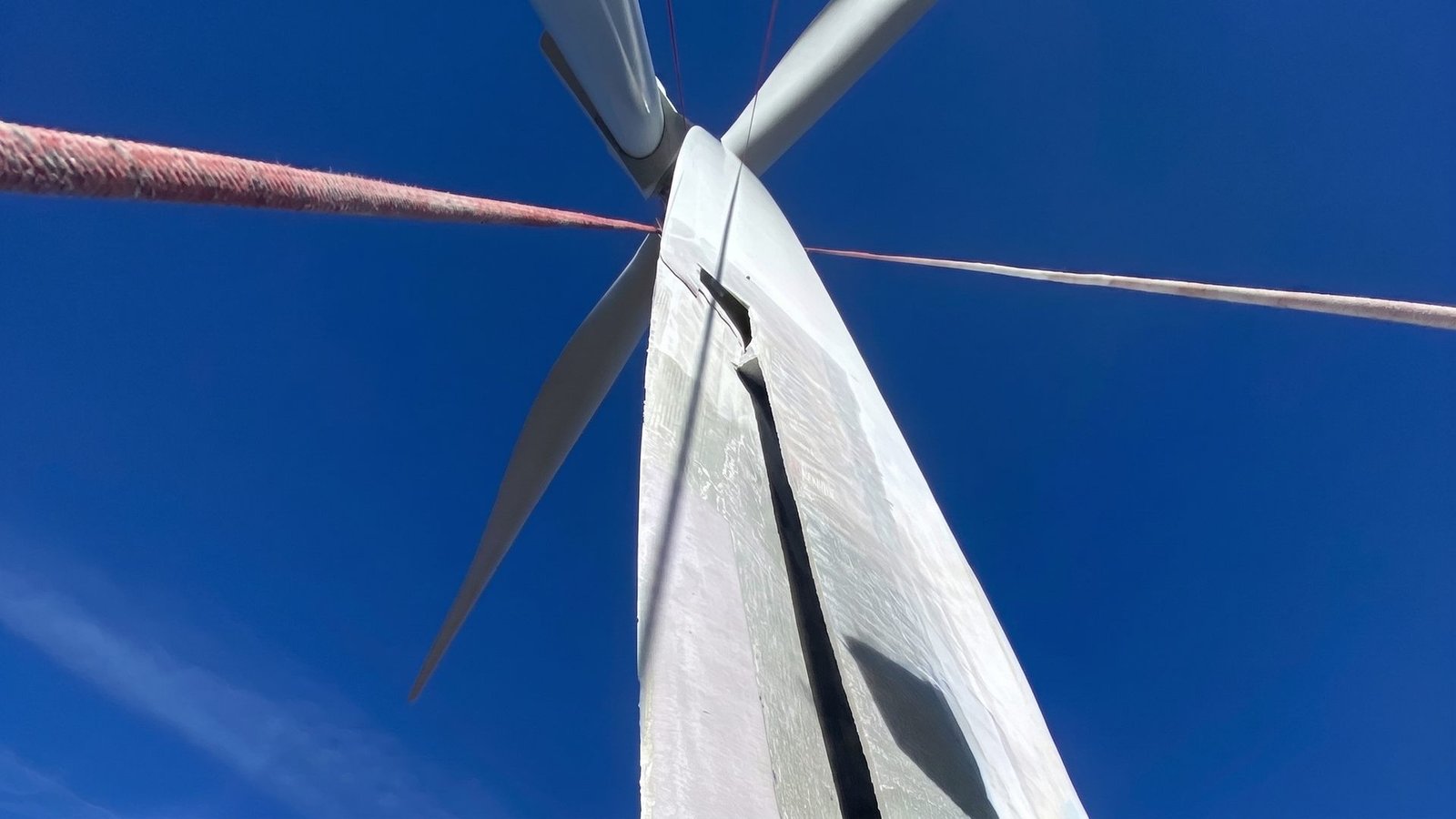 View from below of a wind turbine rotor showing structural leading edge damage on one blade.