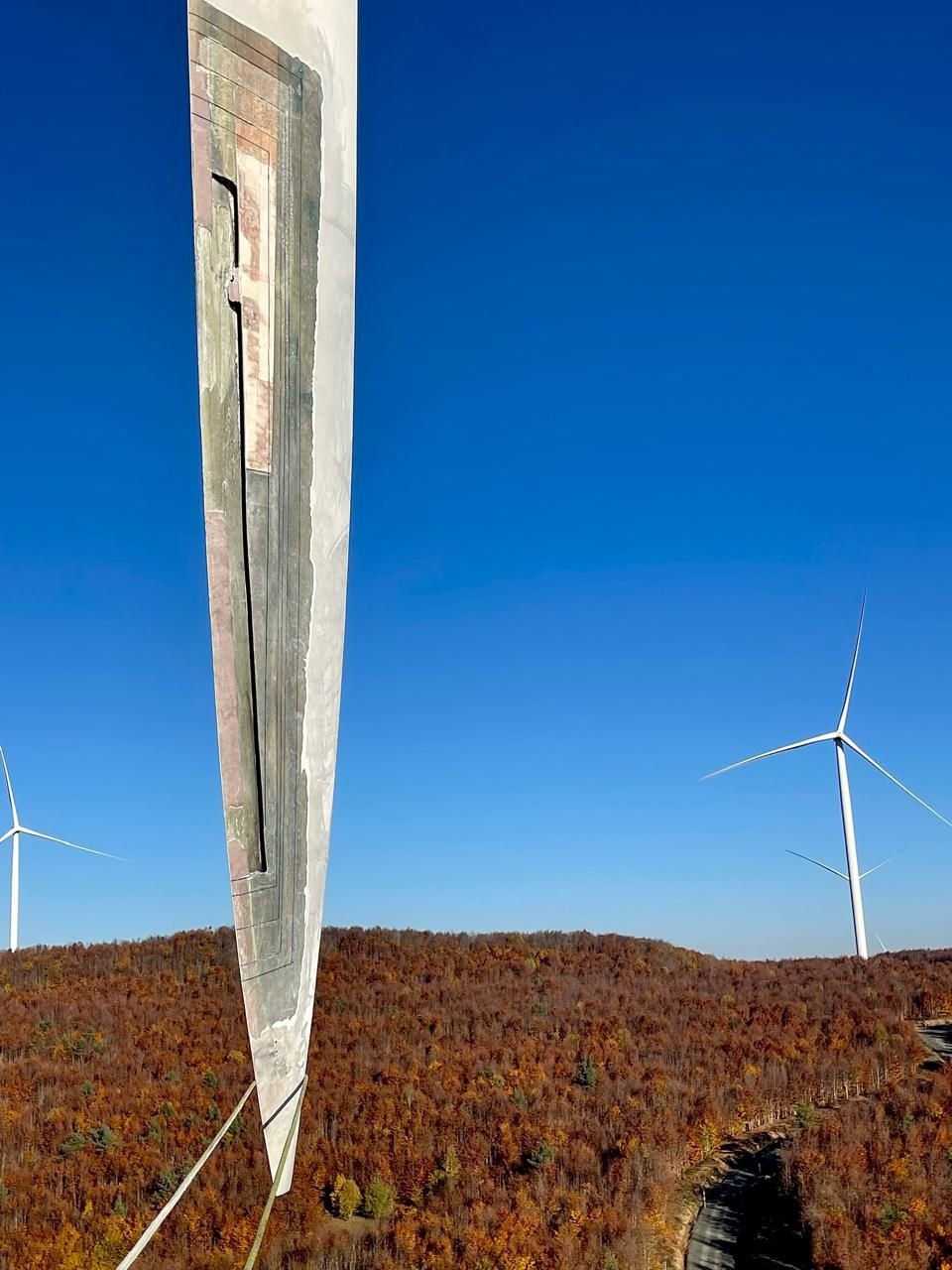 Close-up of a wind turbine rotor blade tip showing leading edge damage, with a wind farm in the background.